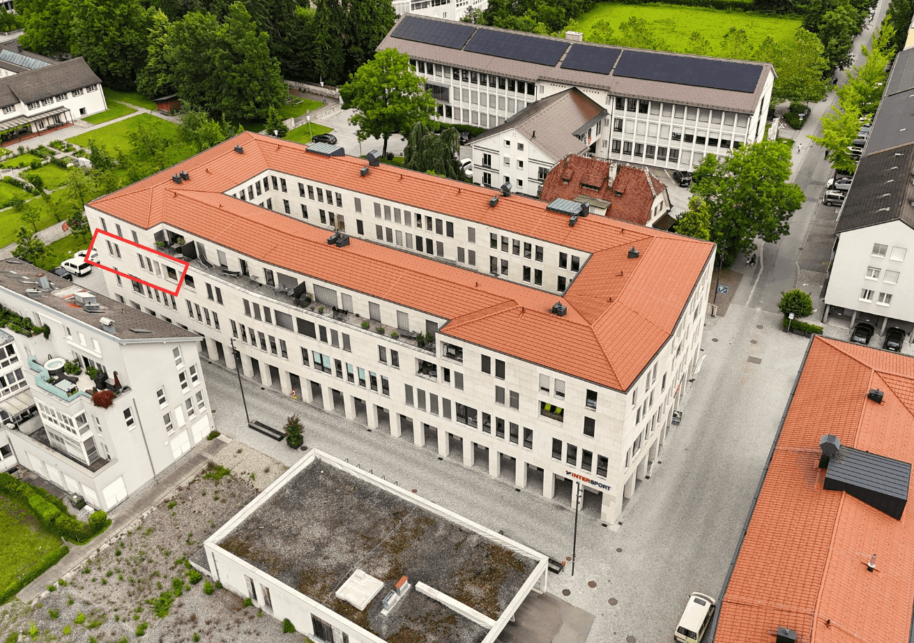 Luftaufnahme eines modernen Wohnkomplexes mit rotem Dach und umliegender Grünfläche.