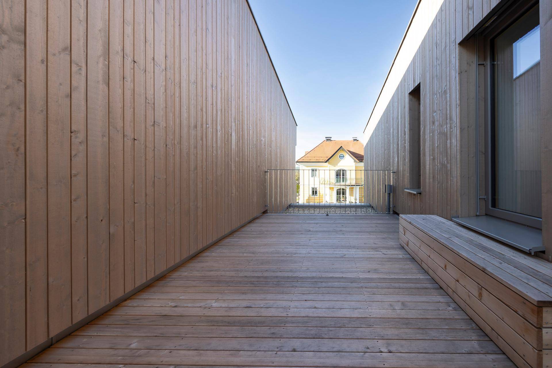 Holzterrasse mit Geländer und Blick auf die benachbarten Häuser.