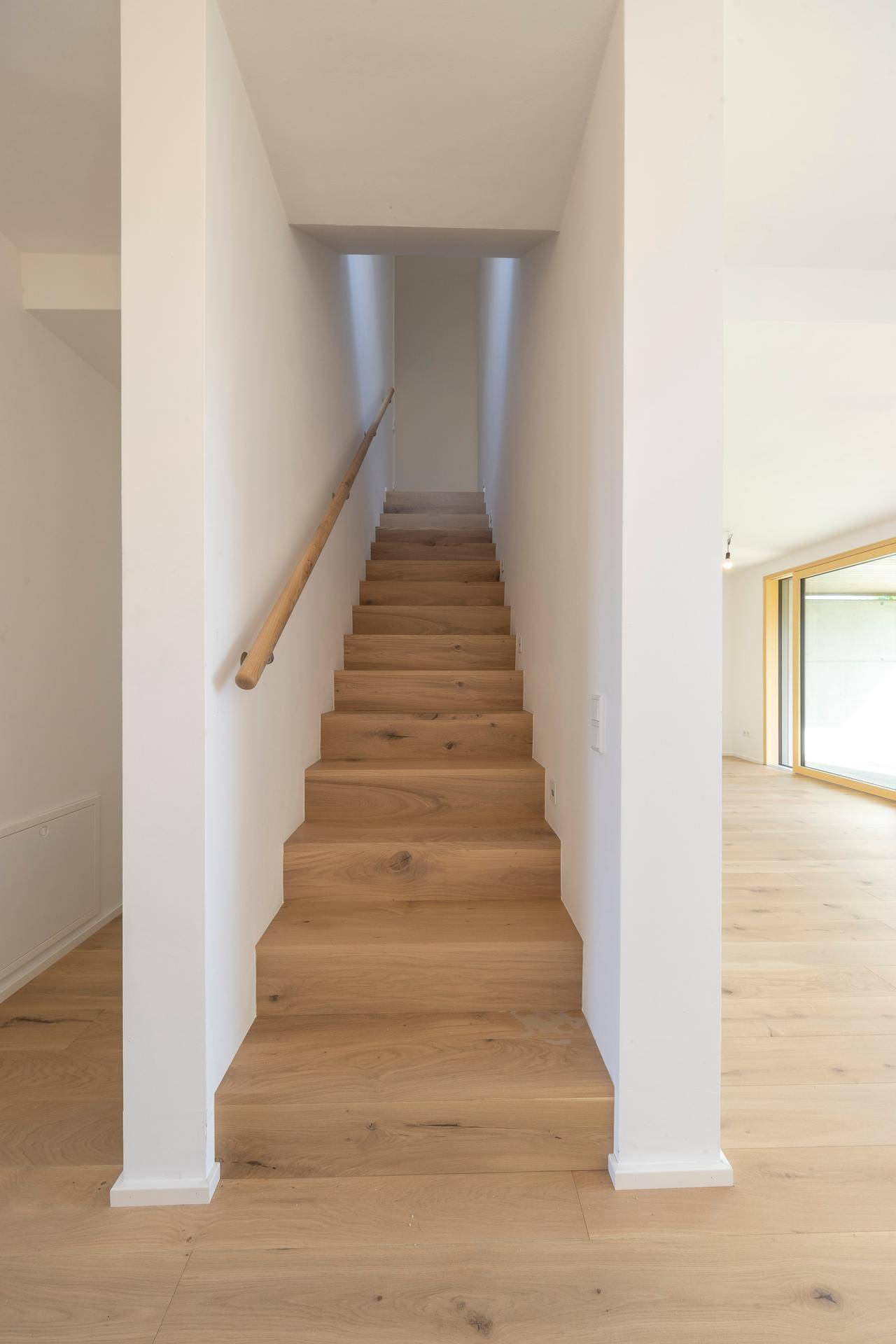 Heller Treppenaufgang mit Holzstufen und schlichtem Holzgeländer.