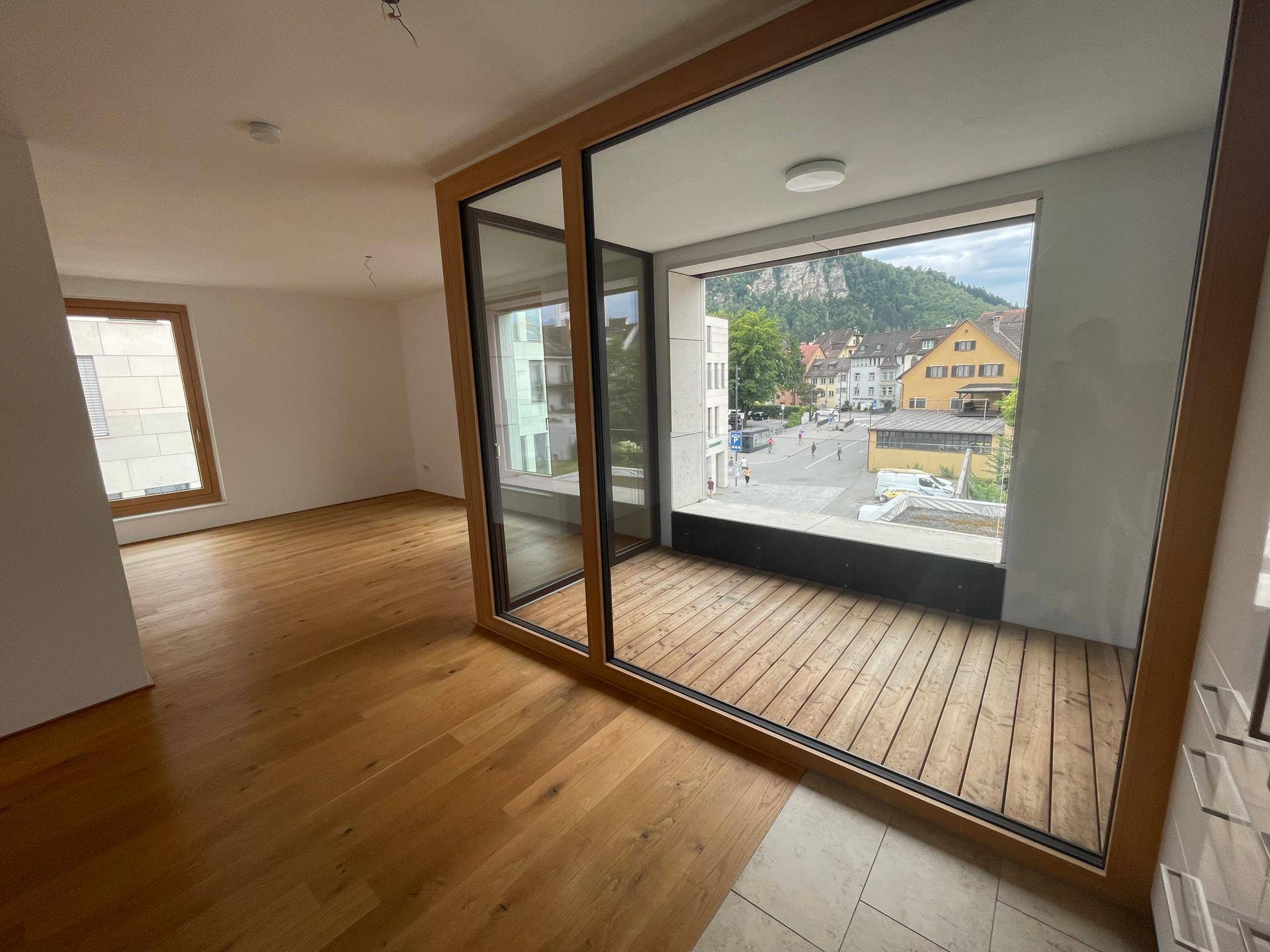 Geräumiger Wohnbereich mit Holzboden und Zugang zu einem Balkon mit Stadt- und Bergblick.