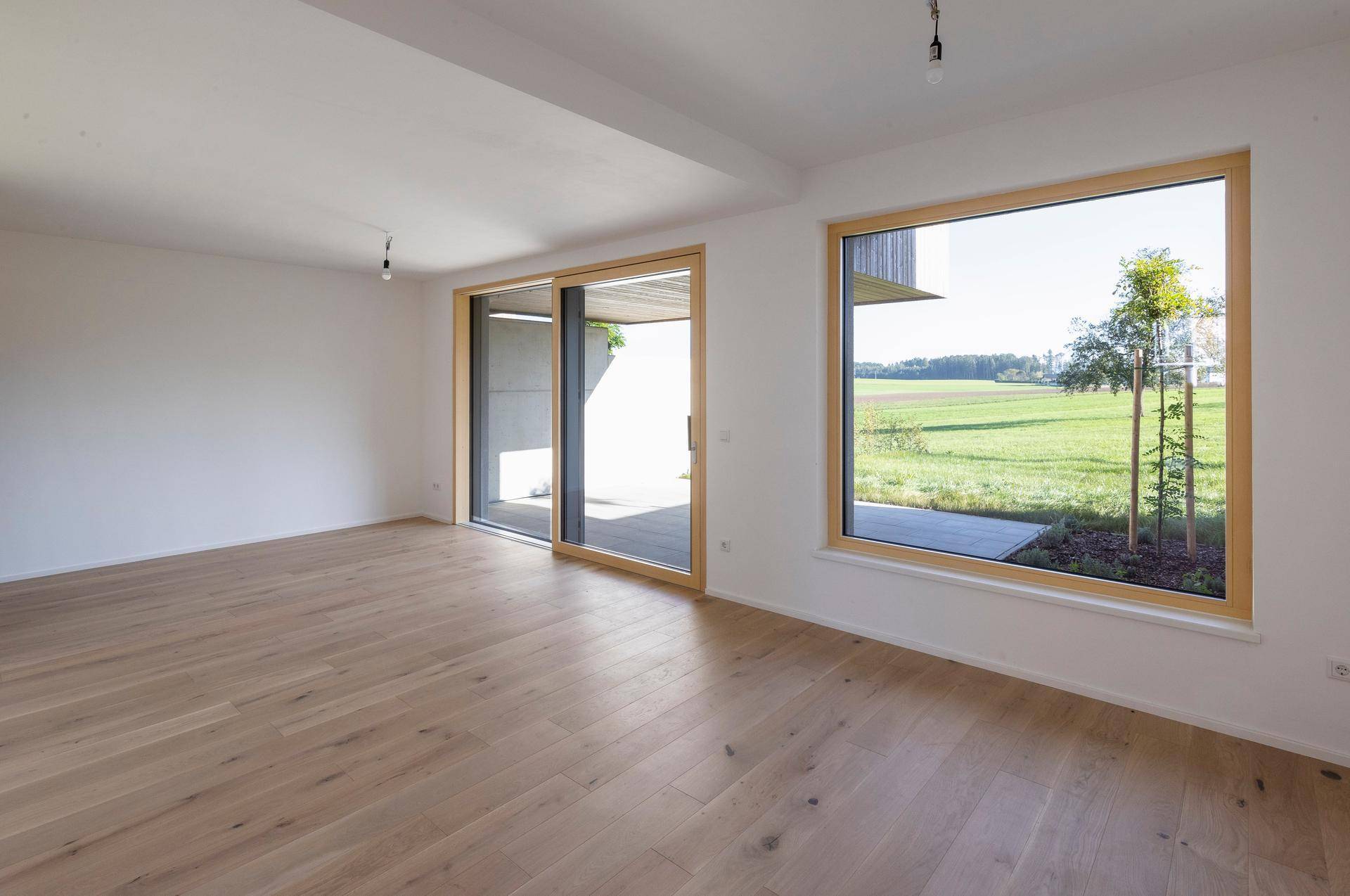 Geräumiger Wohnbereich mit Holzboden und weitem Blick ins Grüne.