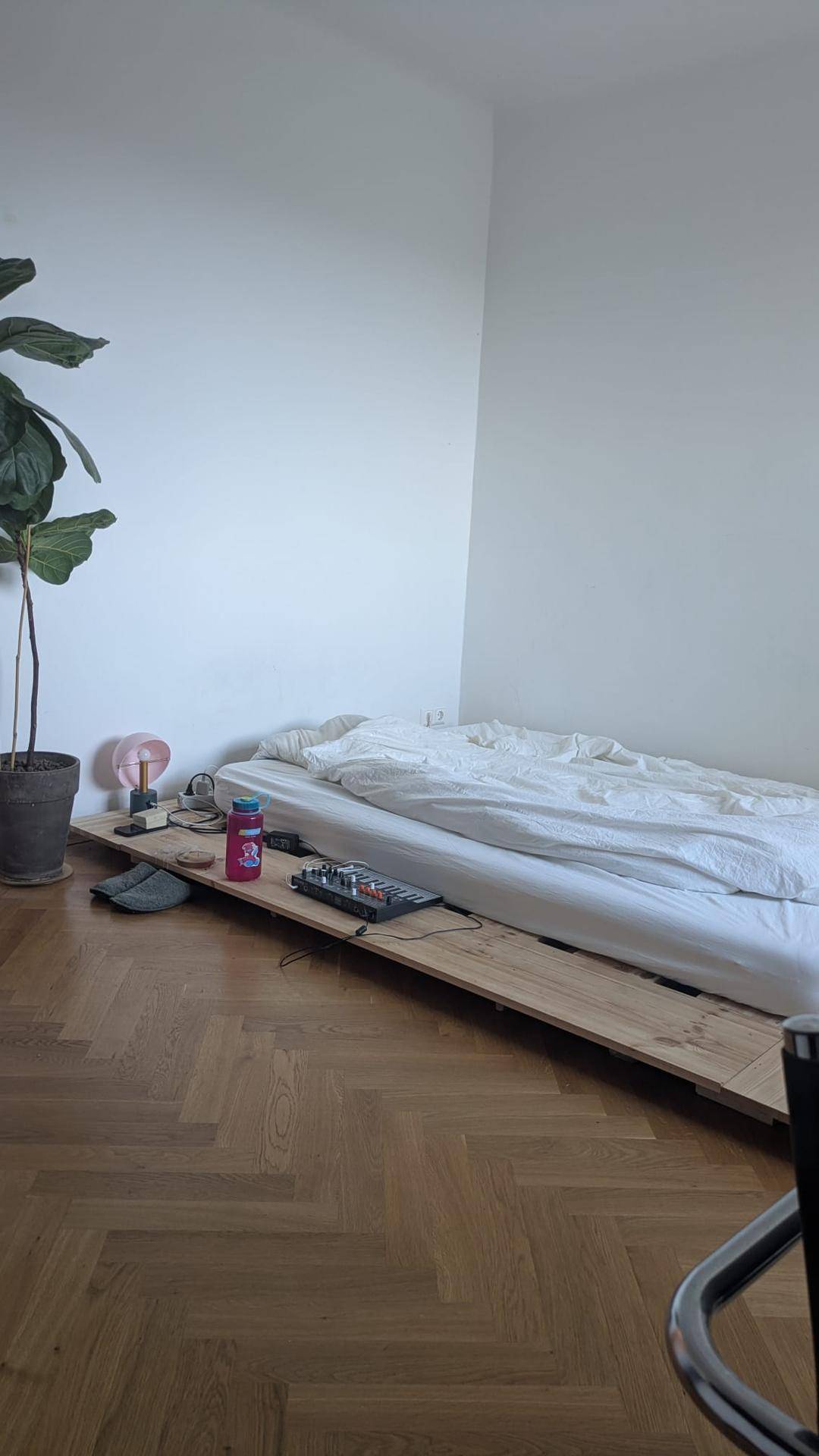 Schlafzimmer mit einem Bett auf einem Holzpodest und hellem Fischgrätparkett.