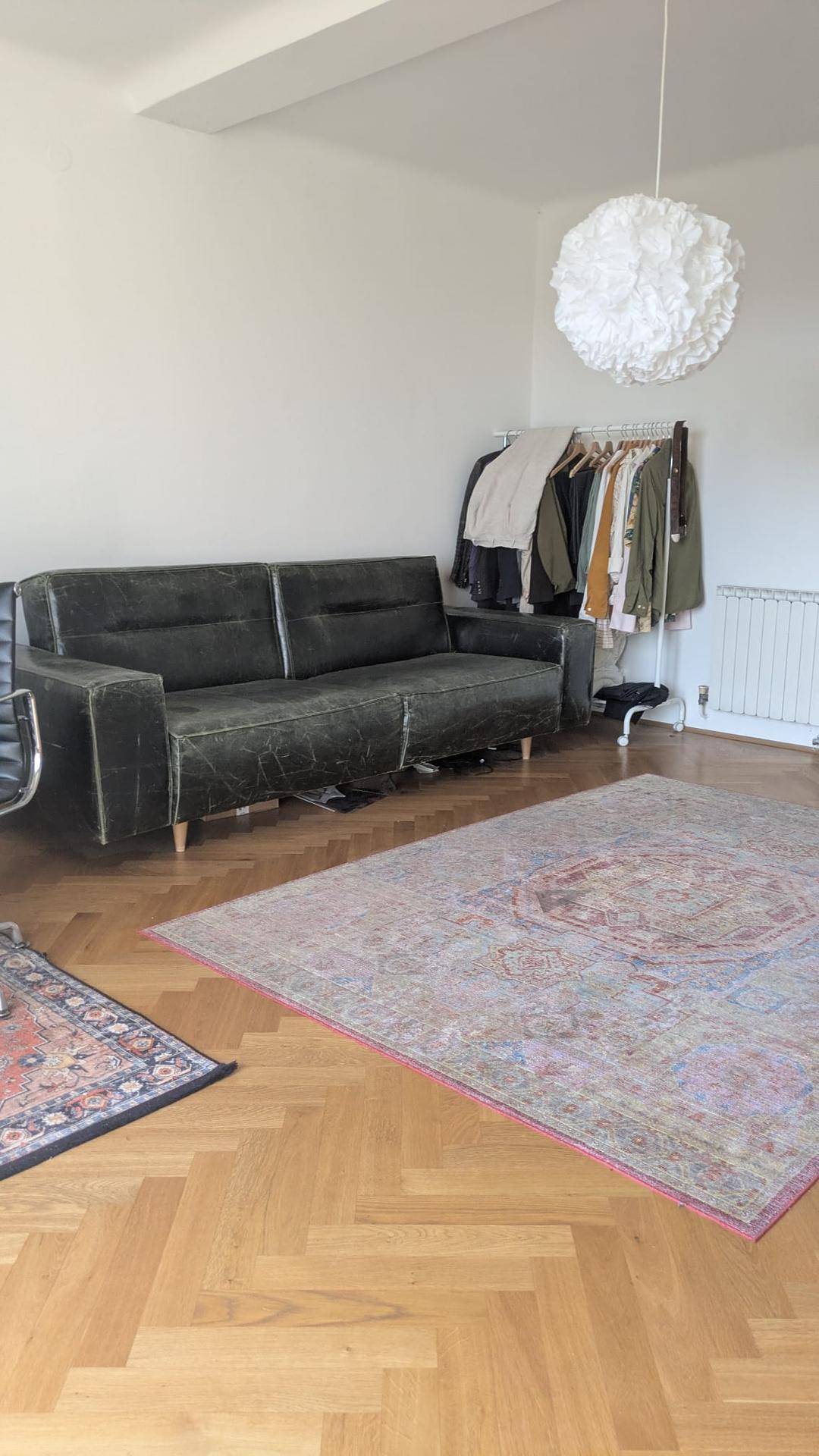 Geräumiges Wohnzimmer mit dunklem Sofa, großem Teppich und hellem Fischgrätparkett.