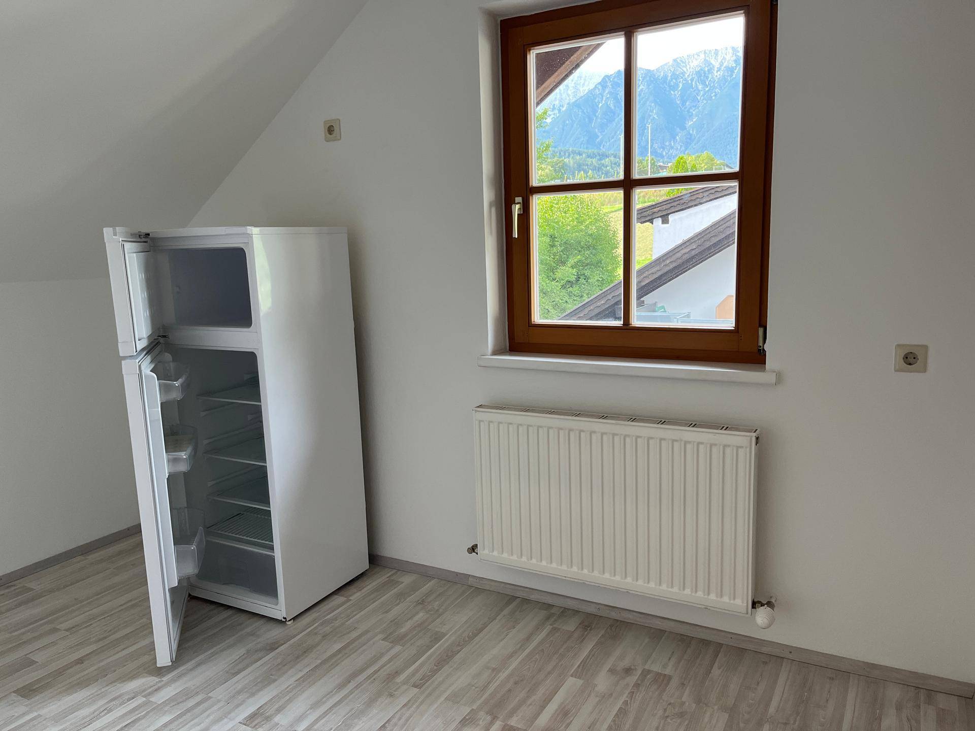 Helles Zimmer mit Kühlschrank, Fenster und Heizkörper, bietet einen schönen Bergblick.
