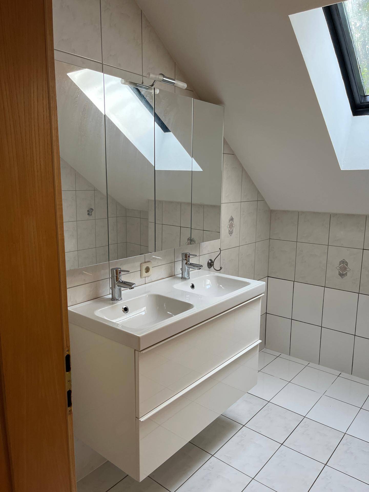 Helles Badezimmer im Dachgeschoss mit Doppelwaschbecken, Spiegelschrank und Dachfenster.