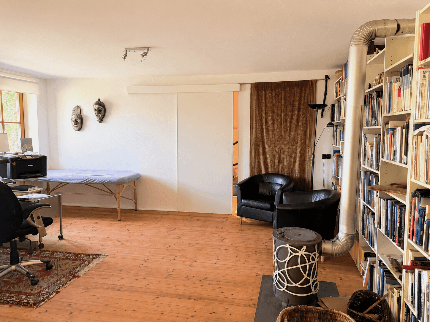 Geräumiges Arbeitszimmer mit Holzdielenboden, Bücherregalen und einem modernen Holzofen.