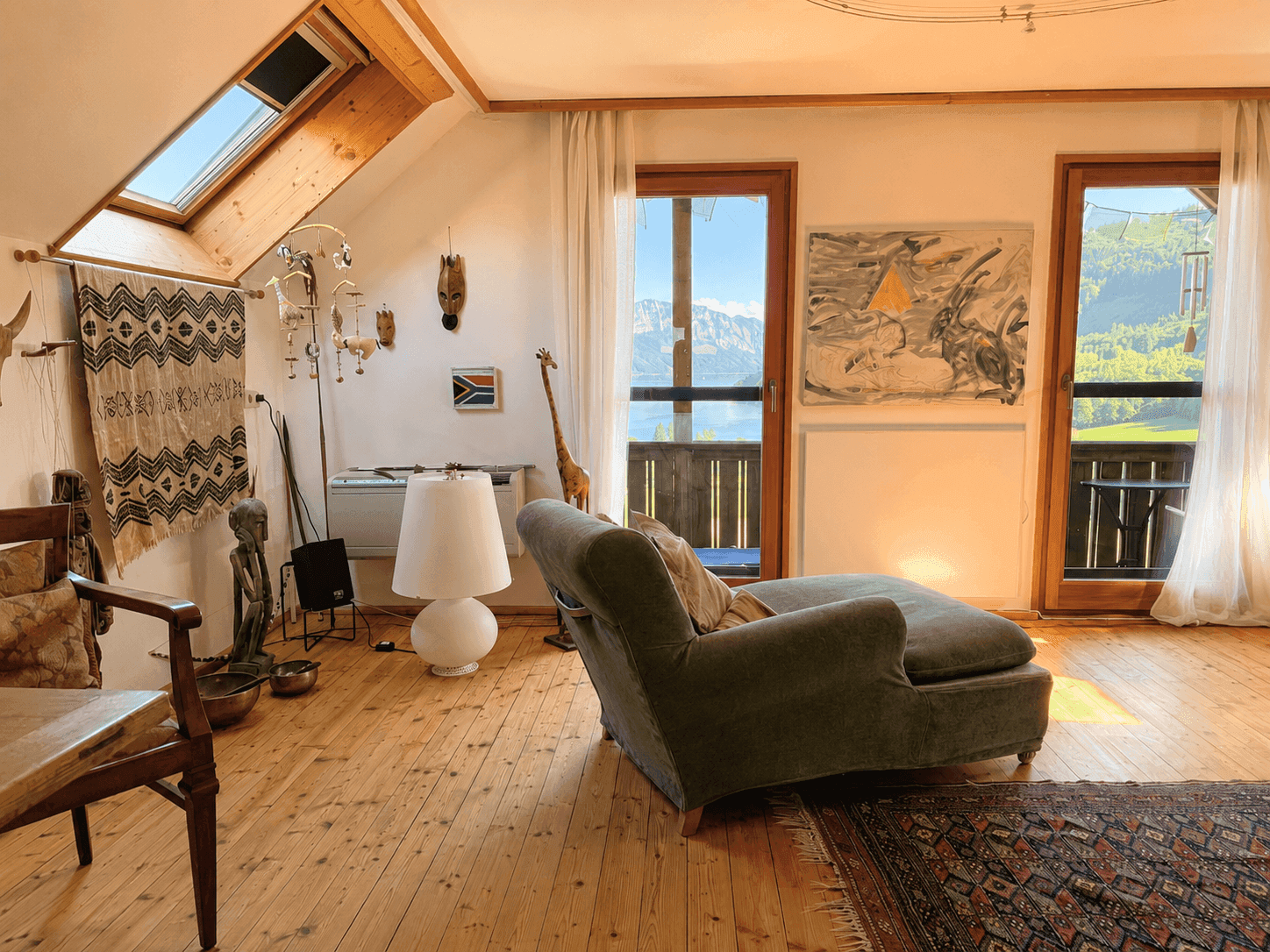 Heller Wohnbereich mit Holzdielenboden, Dachschräge, Oberlicht und Zugang zu einem Balkon mit Aussicht.