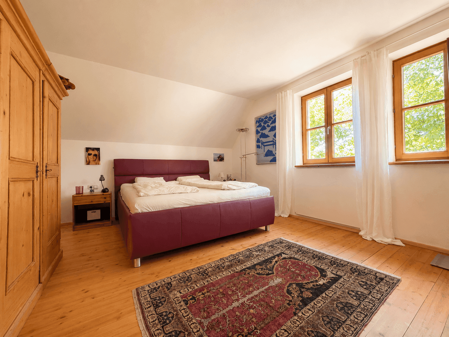 Helles Schlafzimmer mit Holzdielenboden, großem Bett und Holzschrank unter einer Dachschräge.
