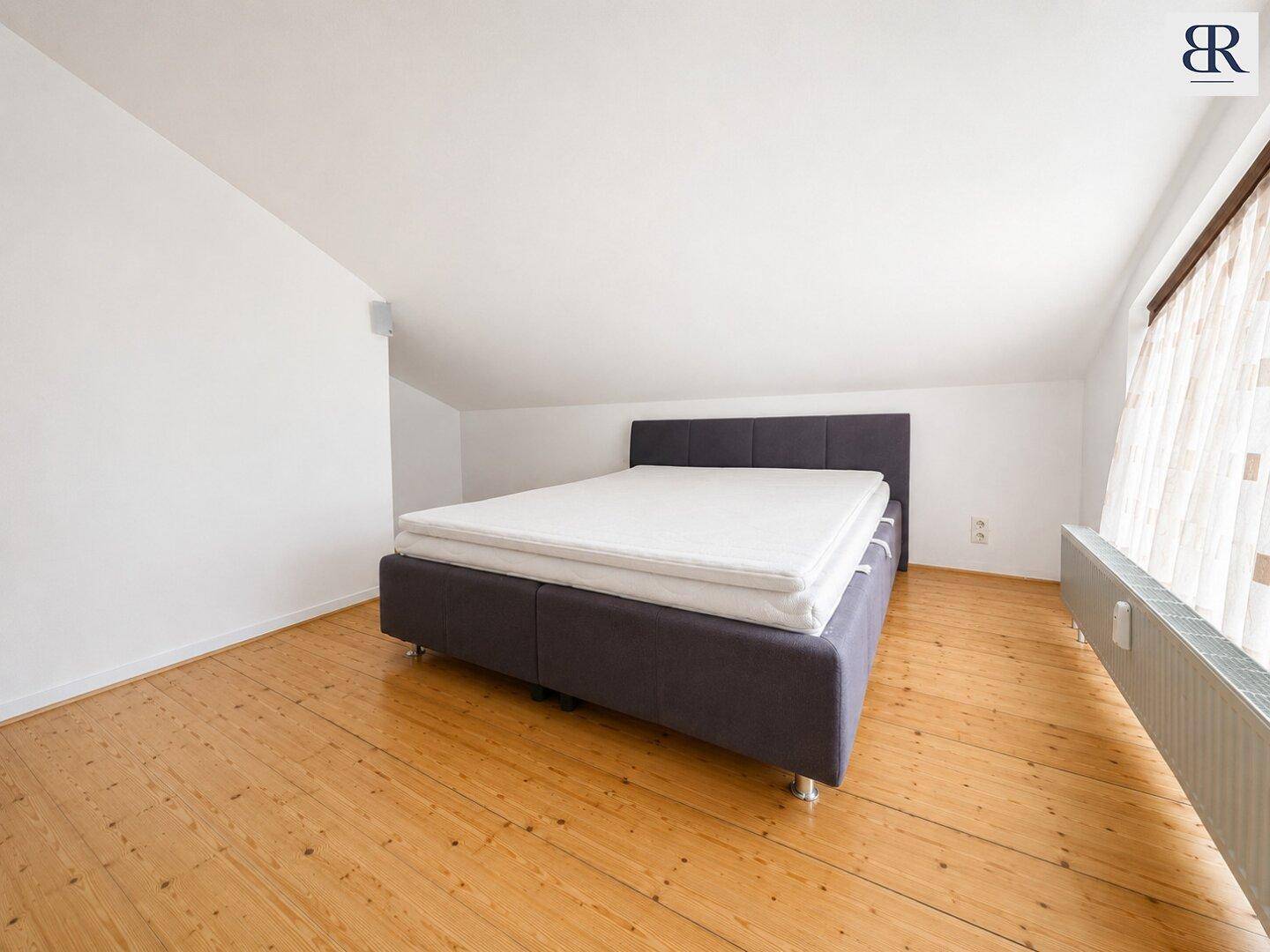 Helles Schlafzimmer mit Holzboden, großem Bett und Dachschräge, bietet eine gemütliche und ruhige Atmosphäre.