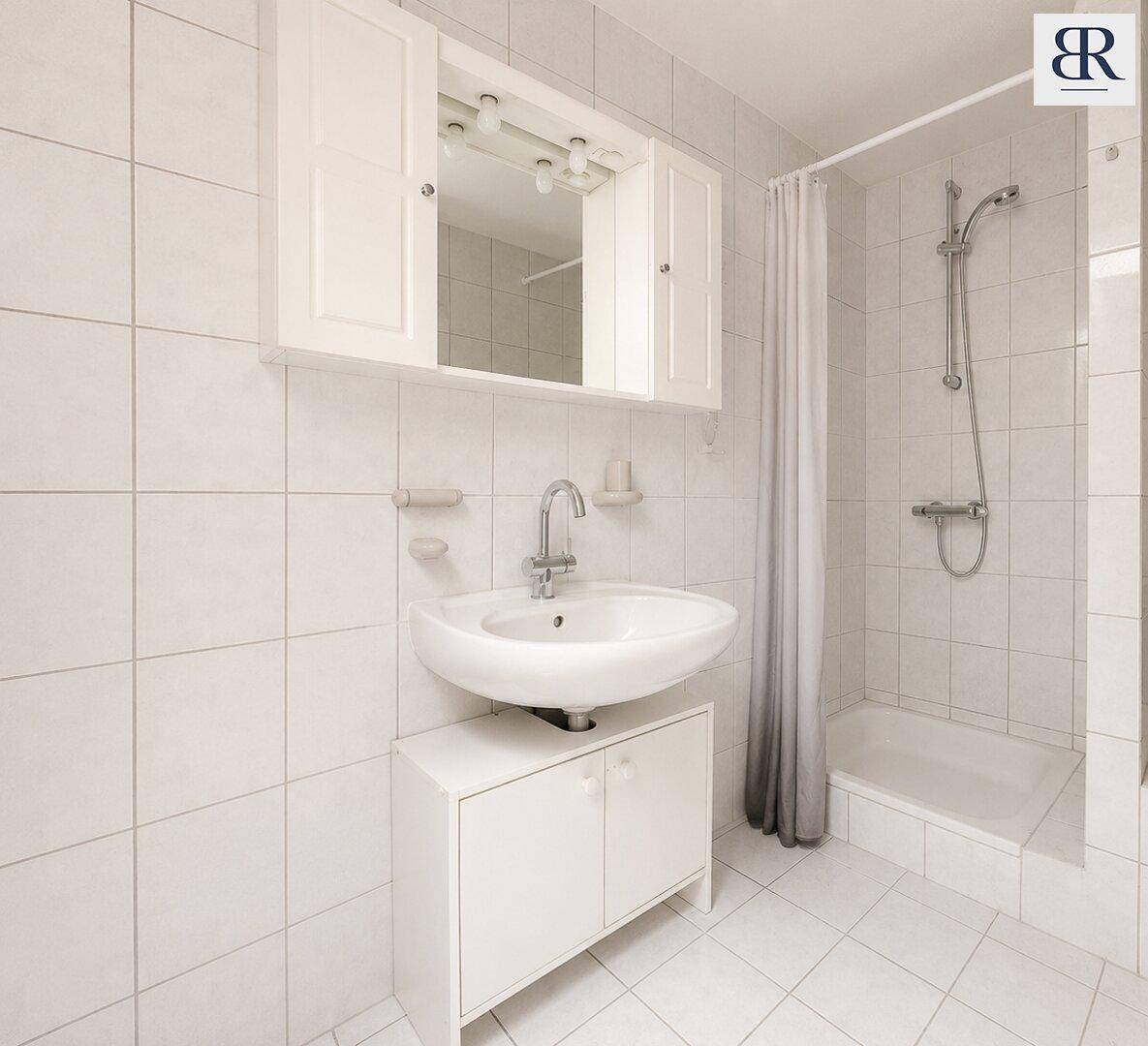 Funktionales Badezimmer mit weißen Fliesen, Waschbecken, Spiegelschrank und Duschbereich für den täglichen Gebrauch.