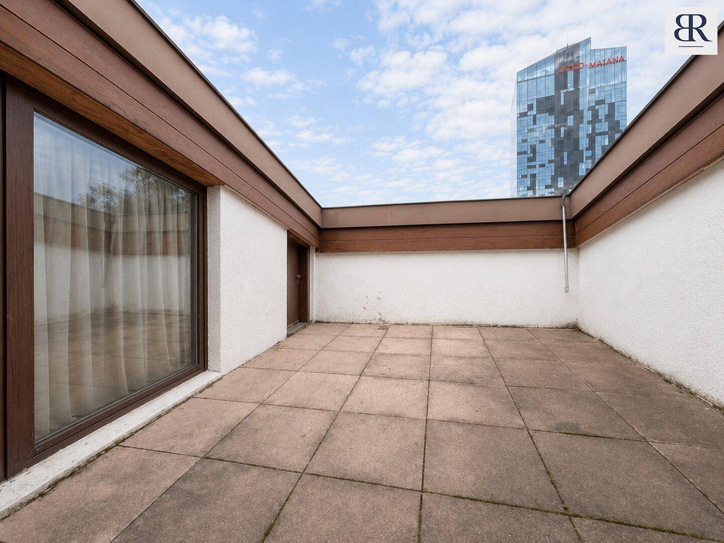 Geräumige Terrasse mit Fliesenboden und Blick auf die umliegende Stadtbebauung, perfekt für Entspannung im Freien.