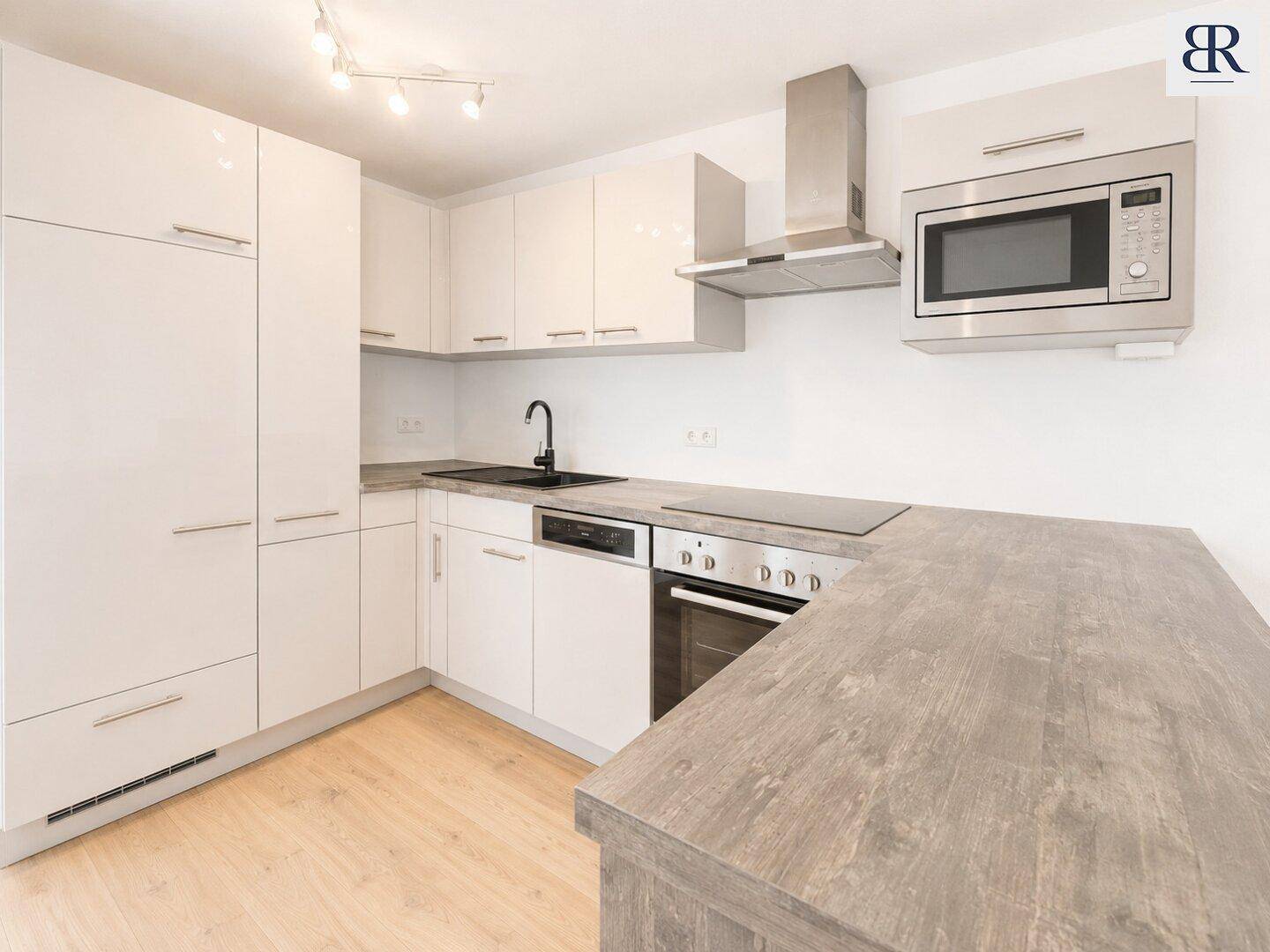 Moderne Einbauküche mit weißen Hochglanzfronten, integrierten Geräten und dunkler Arbeitsplatte für effizientes Kochen.