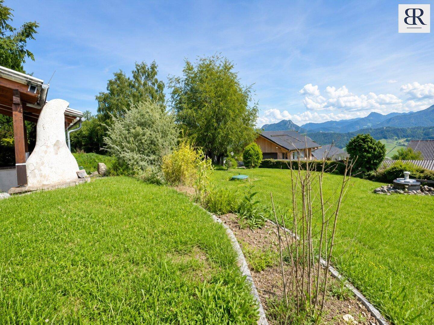 Grüner Gartenbereich mit Rasen, Sträuchern und weitem Blick auf die umliegende Berglandschaft.