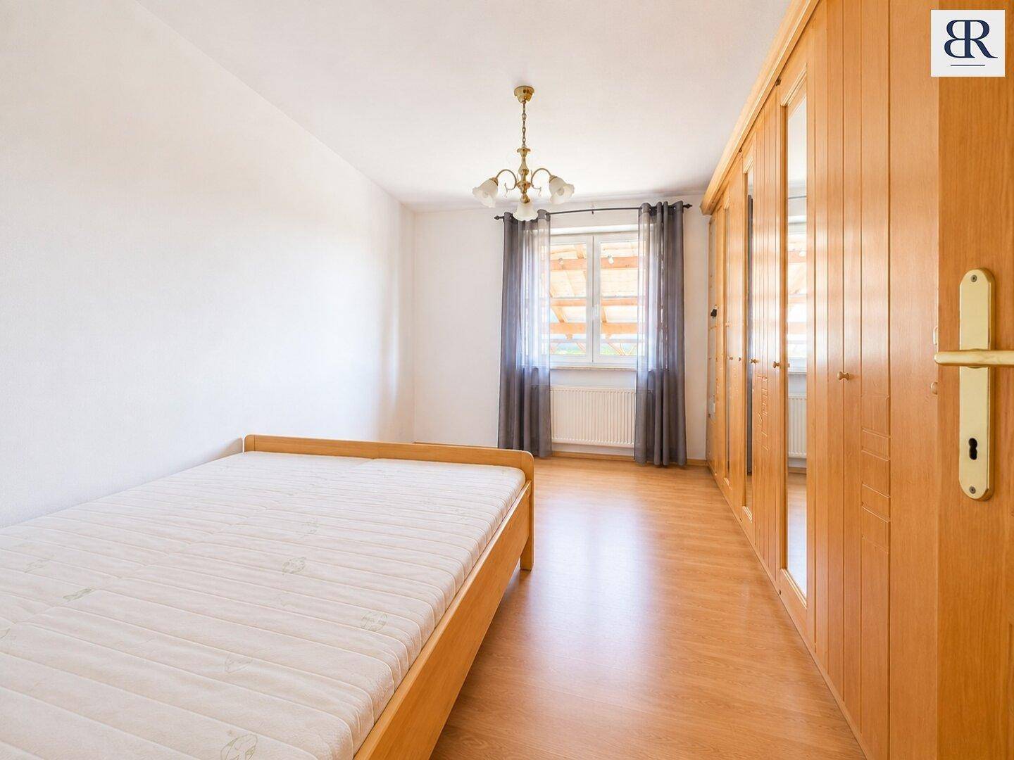Schlafzimmer mit Einzelbett, Holzschrank und Parkettboden, hell und funktional eingerichtet.