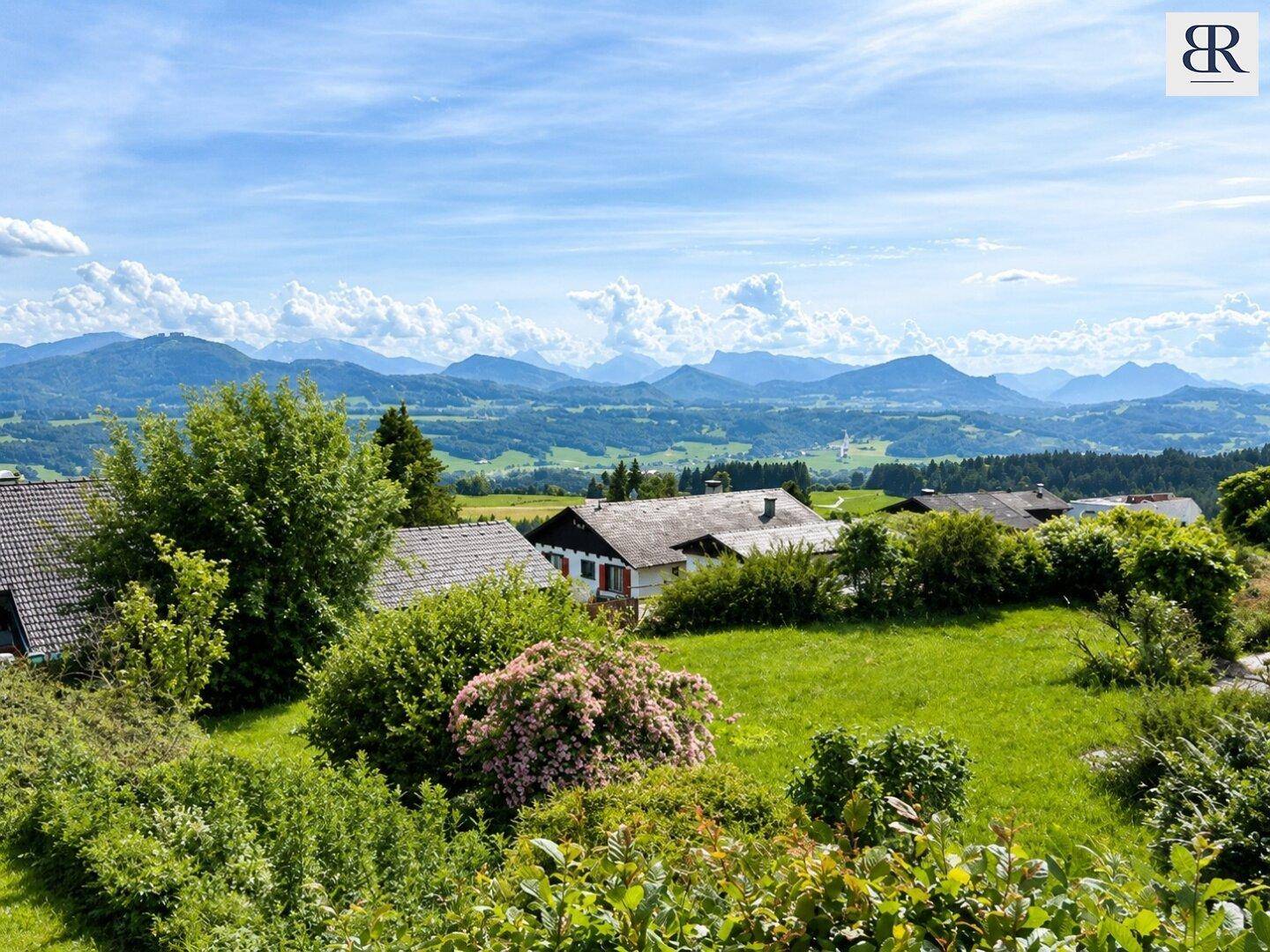 Weitläufiger Panoramablick über eine ländliche Siedlung mit Bergen im Hintergrund unter blauem Himmel.