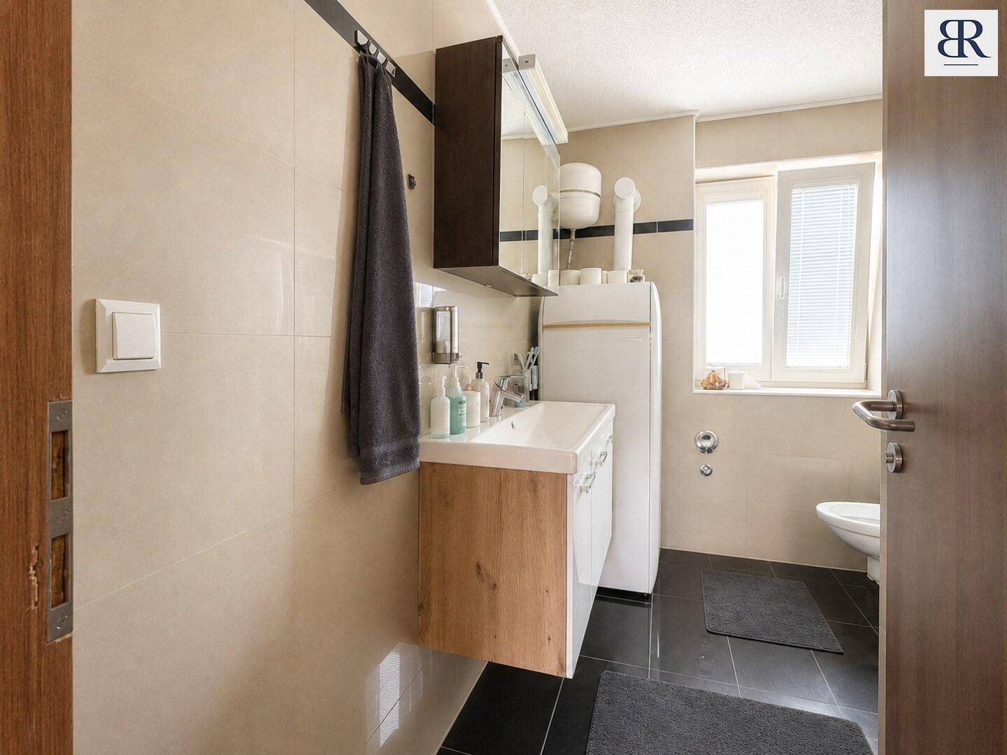 Modernes Badezimmer mit Waschtisch, Spiegelschrank, WC und Fenster für gute Belüftung.