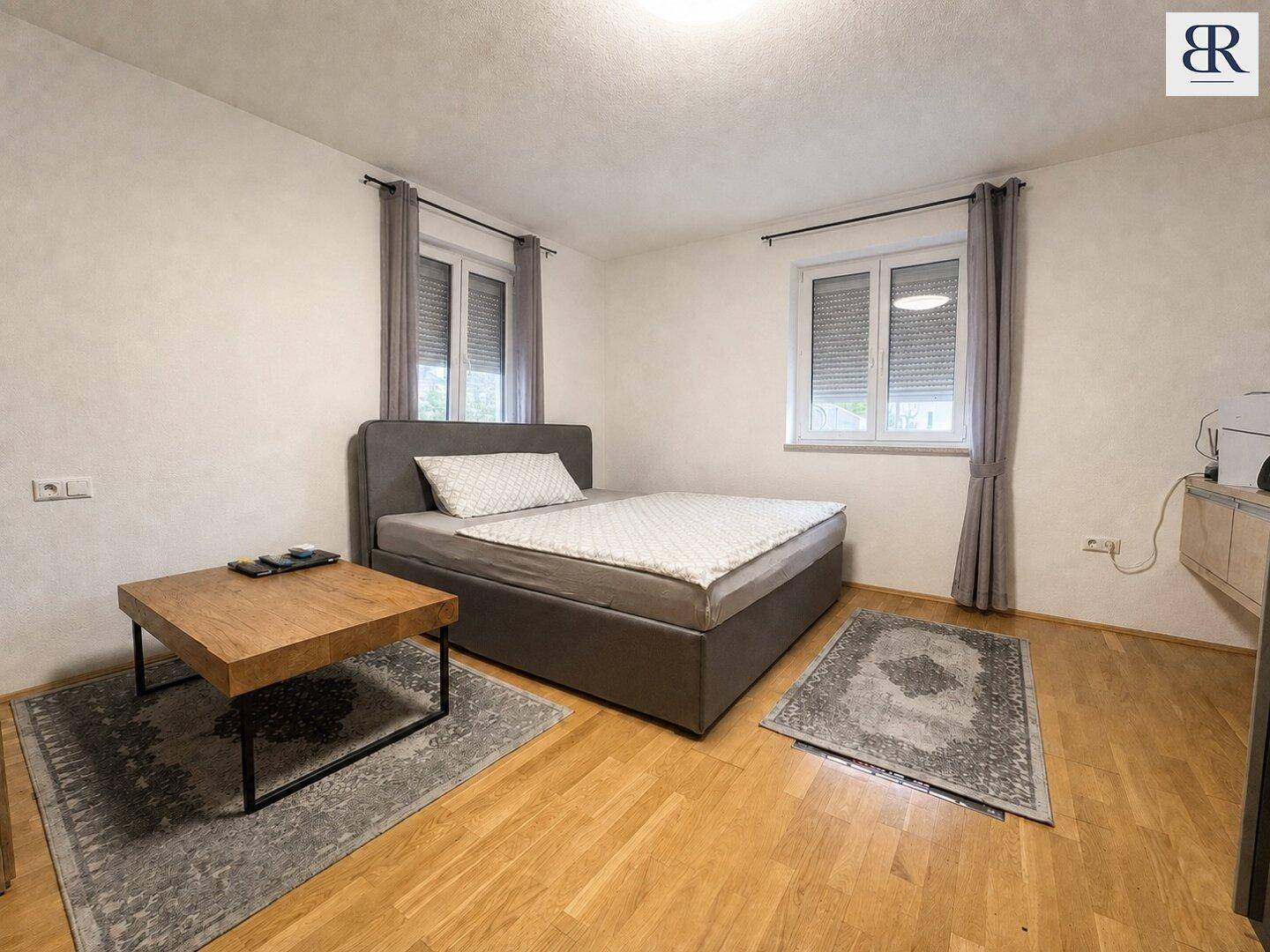 Gemütliches Schlafzimmer mit Doppelbett, Holztisch und zwei Fenstern für natürliches Licht.