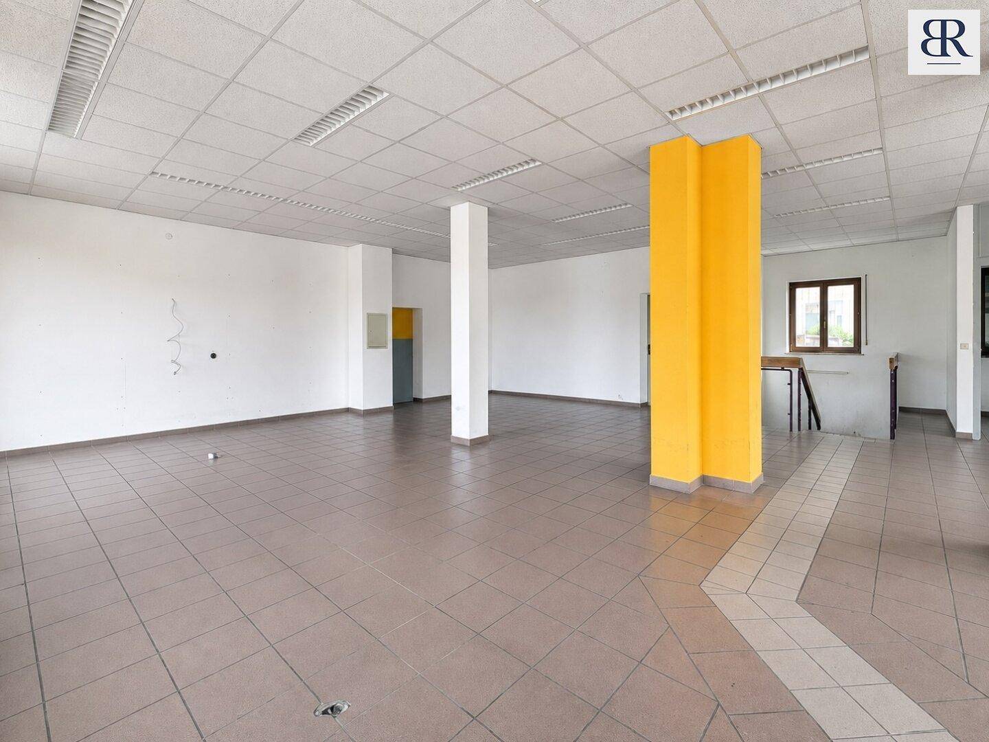 Weiterer Blick in den großen Gewerberaum mit gelben Säulen und einem durchgehenden Fliesenboden.