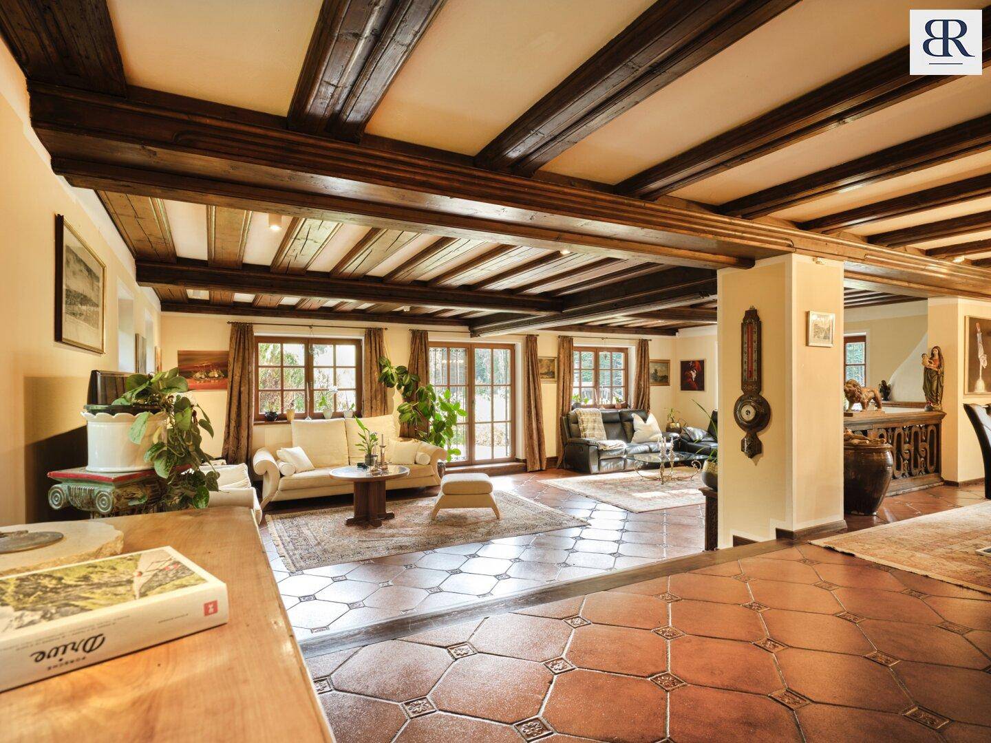 Geräumiges Wohnzimmer mit sichtbaren Holzbalken, Fliesenboden und traditioneller Einrichtung.