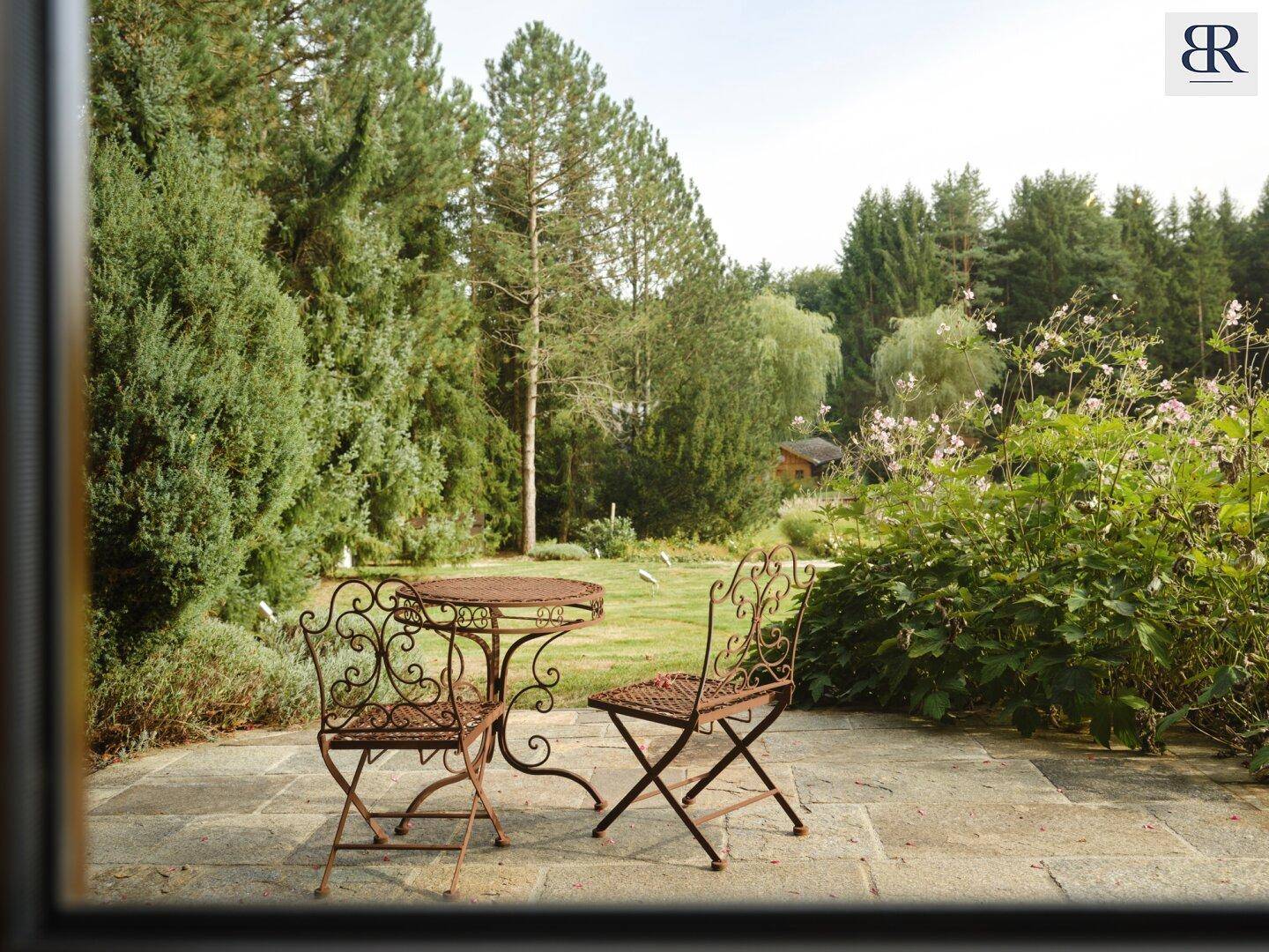 Gemütliche Terrasse mit schmiedeeisernen Gartenmöbeln, umgeben von üppigem Grün und Bäumen.