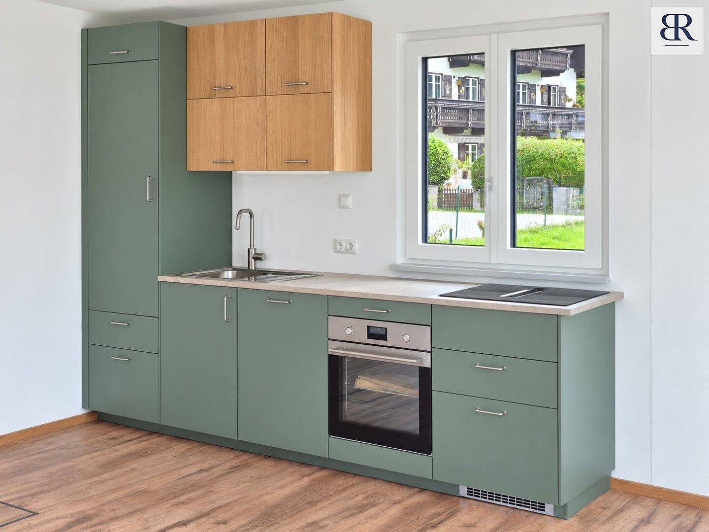 Moderne Küche mit grünen und holzfarbenen Schränken, integriertem Backofen und Induktionskochfeld. Heller Raum mit Fenster und Blick ins Grüne.