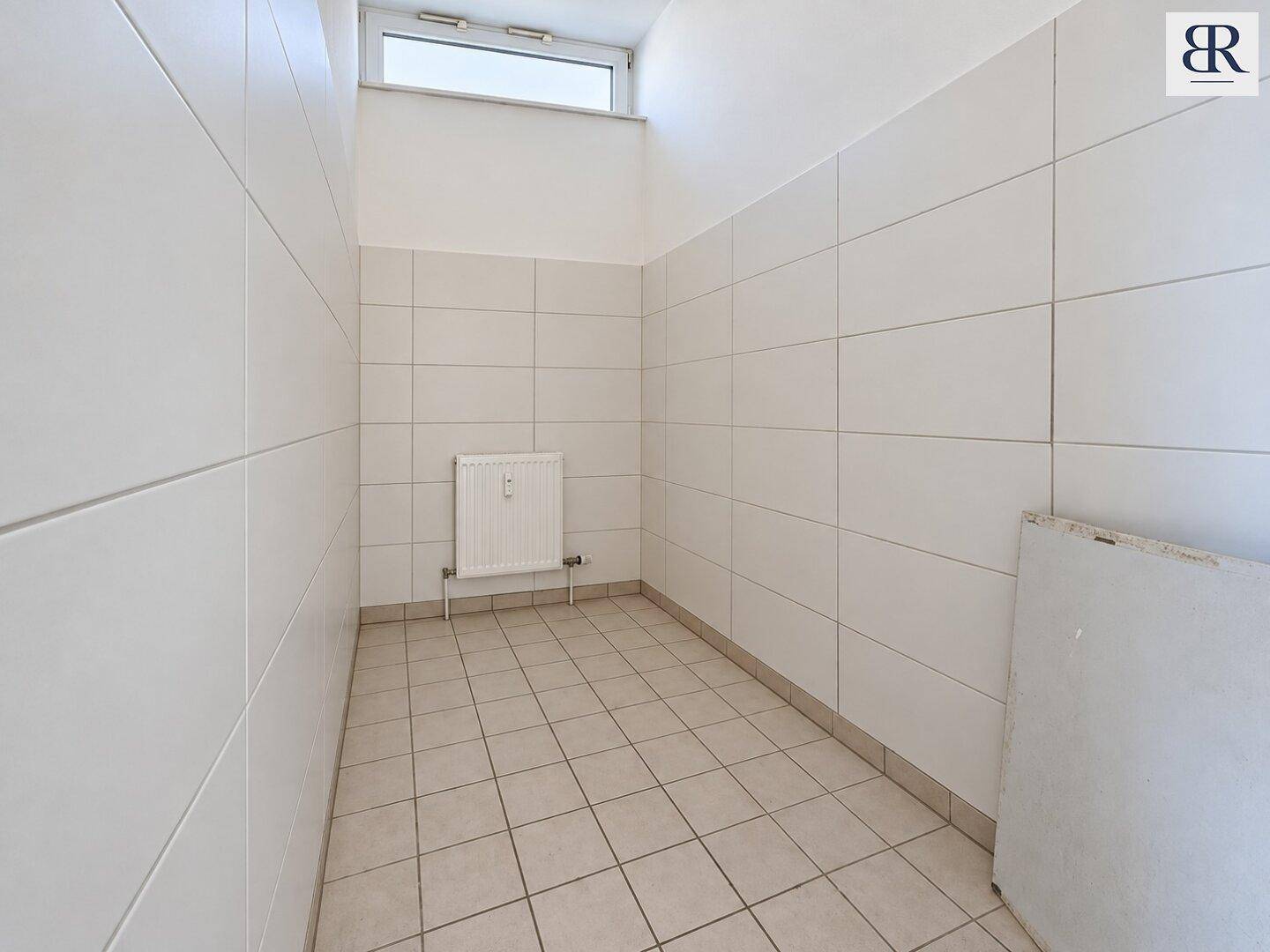 Gefliester Hauswirtschaftsraum mit kleinem Fenster und Heizkörper, in gutem, sauberem Zustand.