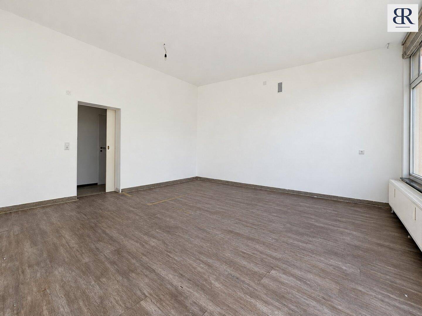 Leerer, heller Gewerberaum mit Laminatboden und weißen Wänden, bereit für die individuelle Gestaltung.