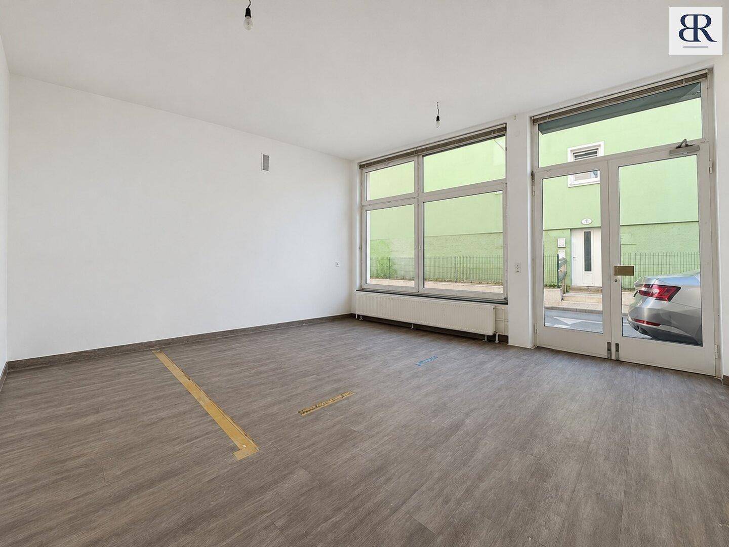 Heller Gewerberaum mit Laminatboden und großen Fenstern sowie einer Glastür zum Außenbereich.