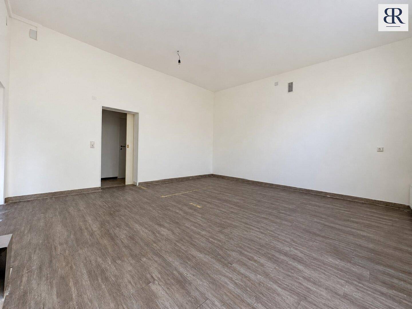 Geräumiger, leerer Raum mit Laminatboden und weißen Wänden, ideal für verschiedene Nutzungskonzepte.