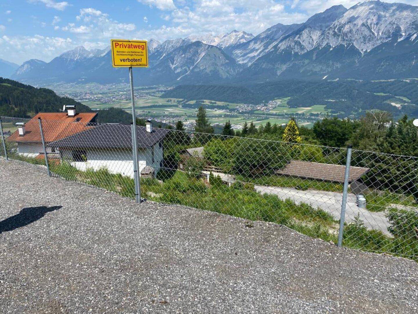 Hinweisschild für Privatweg vor einem Zaun mit atemberaubendem Blick auf die Berglandschaft.
