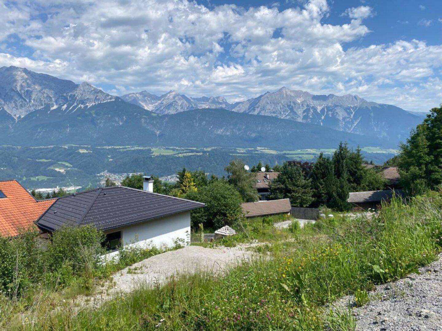 Modernes Wohnhaus mit dunklem Dach, eingebettet in grüne Hügel mit majestätischem Bergpanorama.