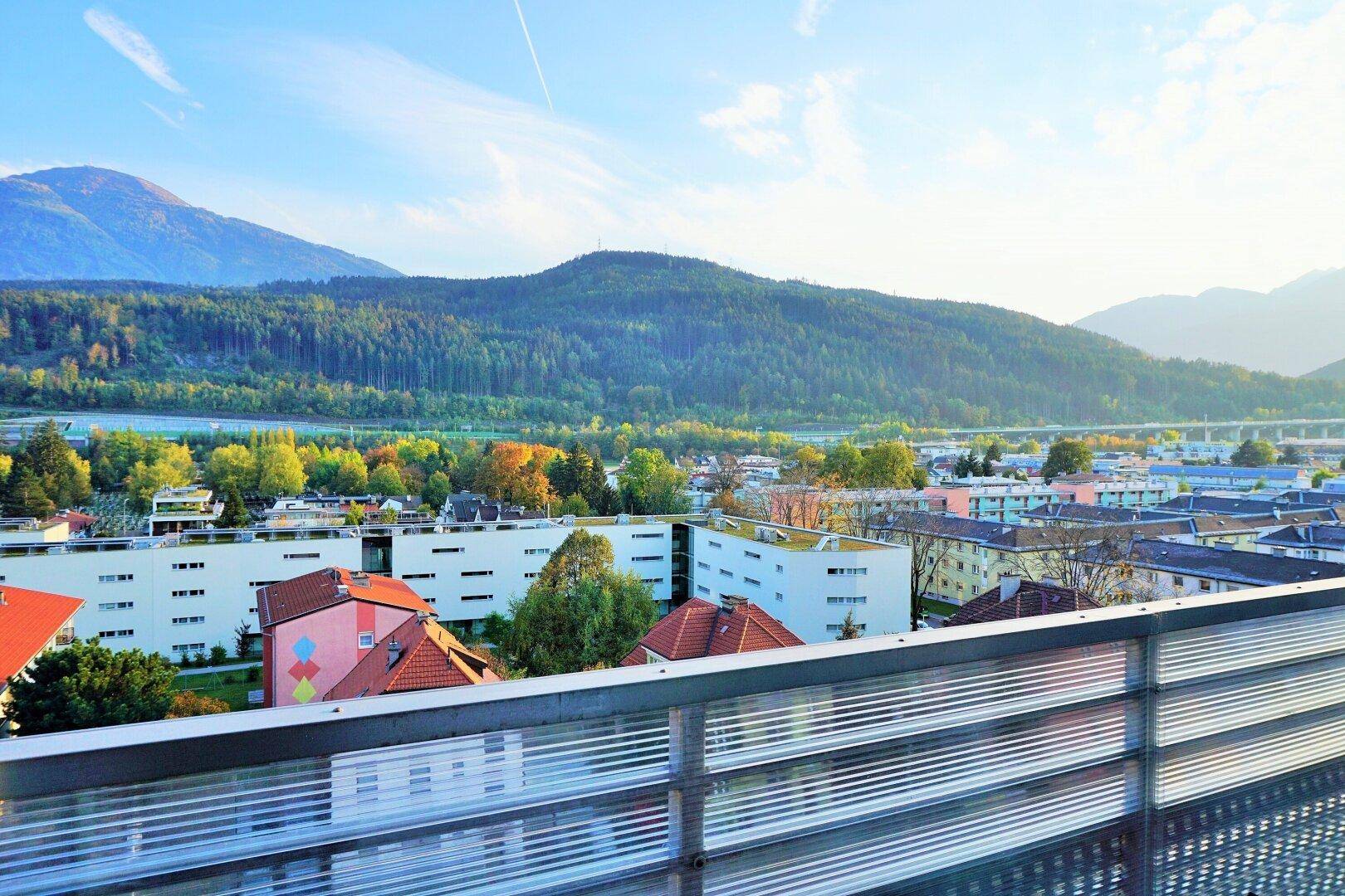 Weitblick über die Stadt und die umliegenden Berge von einem sonnigen Balkon.