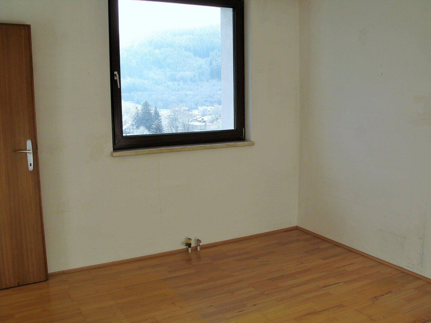 Leeres Zimmer mit Holzfußboden und einem Fenster, das einen weiten Blick bietet.