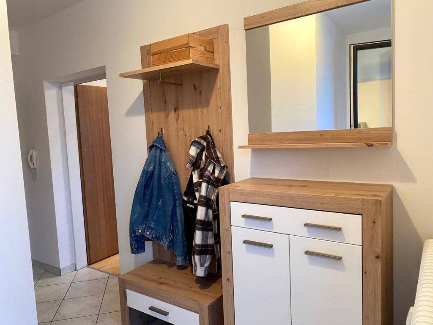 Eingangsbereich mit Garderobe, Spiegel und Schuhschrank in hellem Holzdesign.