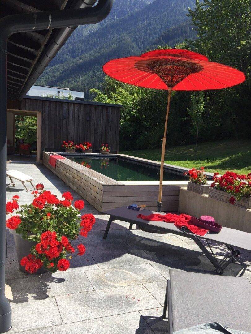 Sonnenterrasse mit Pool, Liegestühlen und rotem Sonnenschirm, ideal zum Entspannen.