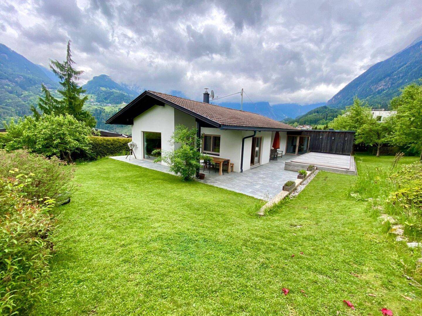 Weitläufiger Garten mit Terrasse und Blick auf die umliegende Berglandschaft unter bewölktem Himmel.