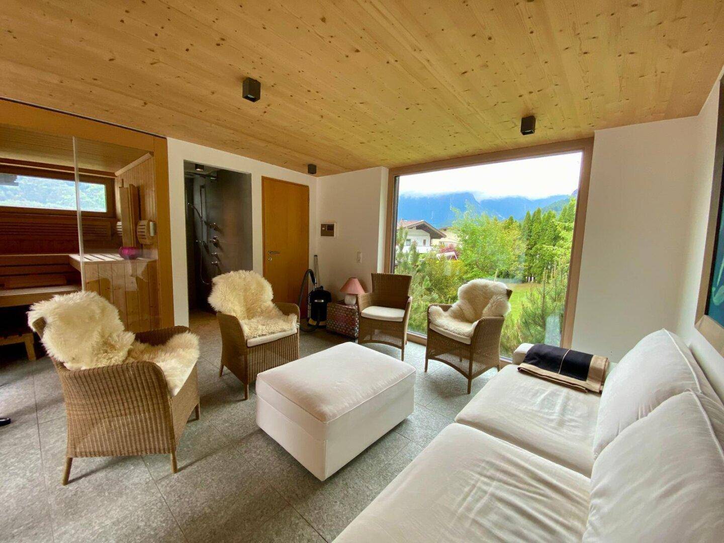 Heller Wohnbereich mit großem Fenster und Blick ins Grüne, angrenzend an eine Sauna.