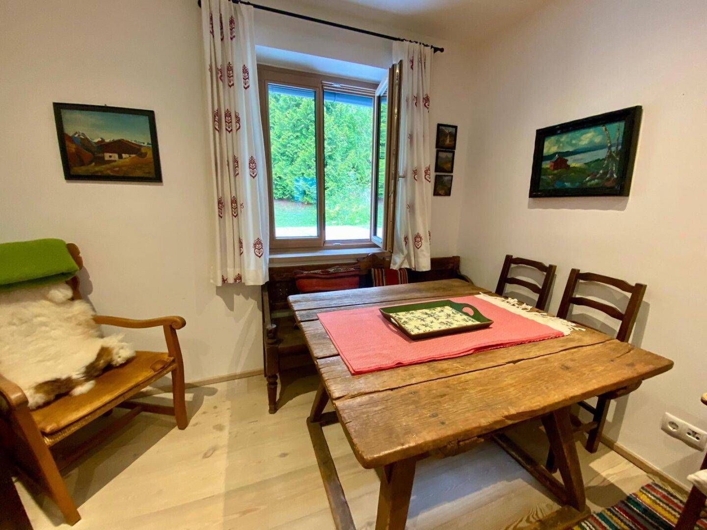 Rustikaler Essbereich mit Holztisch und traditionellen Bildern, bietet Blick in den Garten.