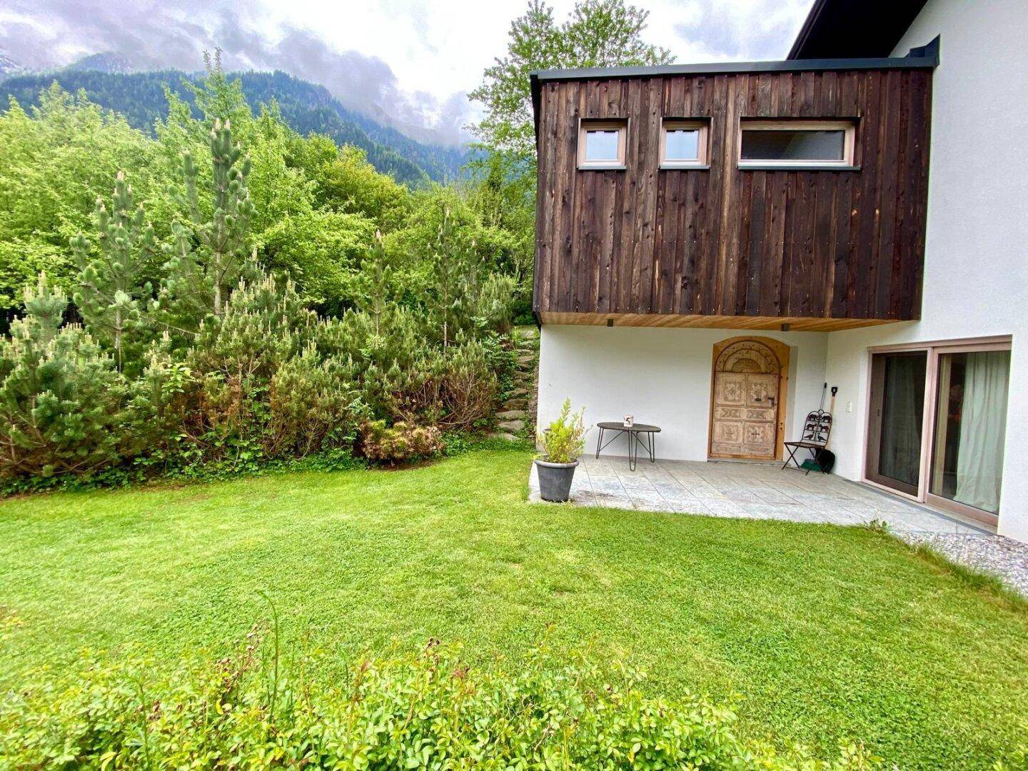 Terrasse mit Garten und Blick auf die bewaldeten Berge, umgeben von grüner Natur.