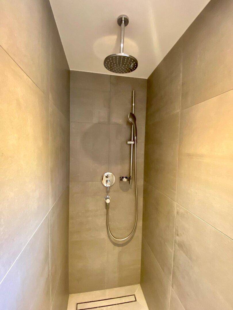 Moderne begehbare Dusche mit Regenduschkopf und grauen Fliesen.