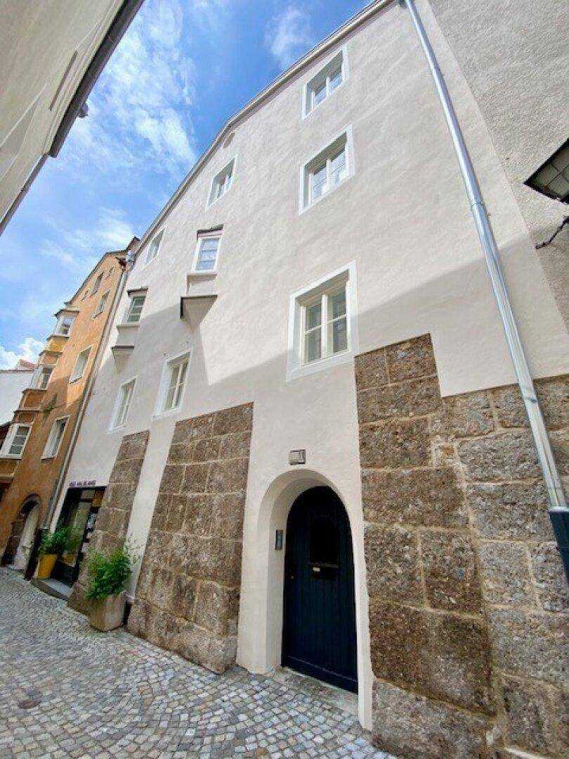 Historische Gebäudefassade mit weißem Putz und Steinsockel in einer engen Gasse.