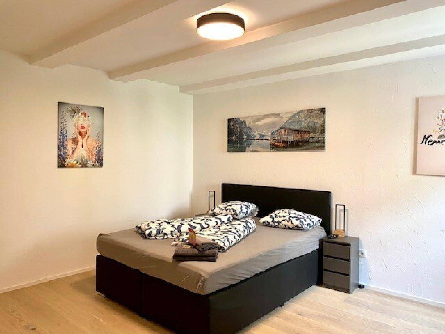 Ruhiges Schlafzimmer mit Doppelbett, Nachttischen und Kunstwerken, unter sichtbaren Deckenbalken.