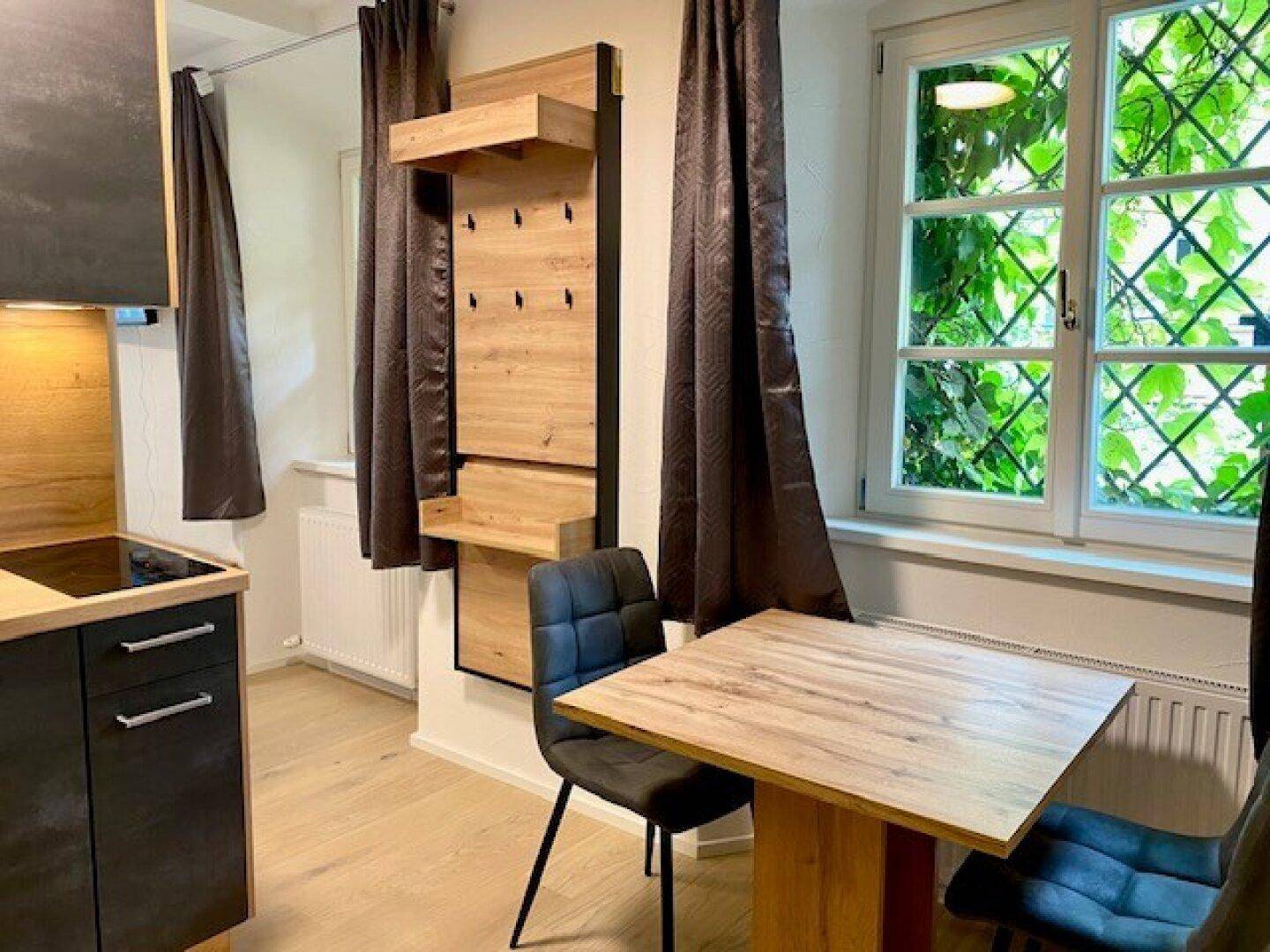 Essbereich mit Holztisch und Stühlen, direkt am Fenster mit Blick ins Grüne, ergänzt durch Garderobe.