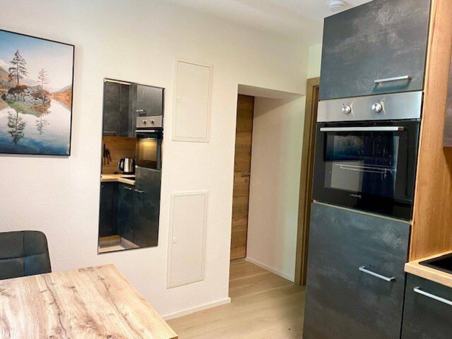 Moderne Küche mit dunklen Schränken, integriertem Backofen und Holzarbeitsplatte, offen gestaltet.