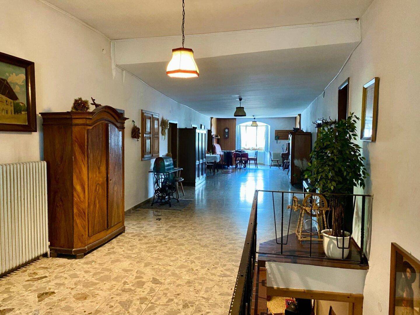 Langer Flur mit traditionellen Holzschränken, gemustertem Fliesenboden und Blick auf einen weiteren Essbereich.