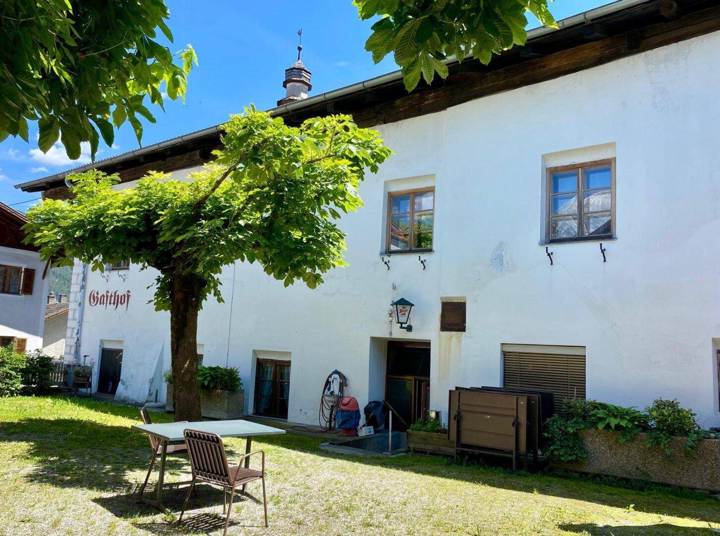 Grüne Gartenfläche neben dem Gebäude mit einem Baum und einem kleinen Tisch mit Stühlen im Freien.