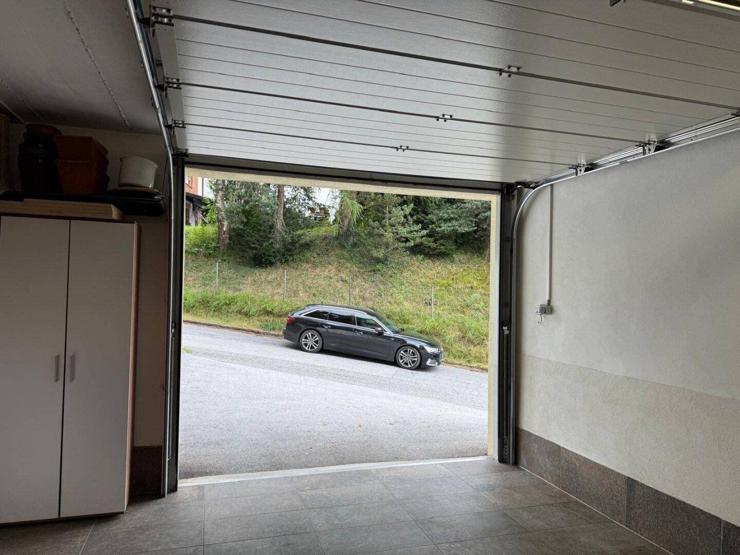 Geräumige Garage mit offenem Tor und Blick auf die Straße und bewaldete Umgebung.