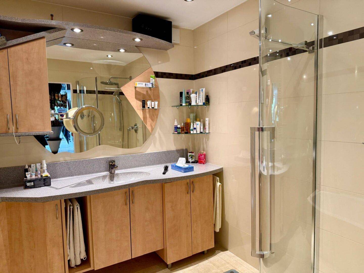 Modernes Badezimmer mit Einzelwaschbecken, Holzschränken und großer Duschkabine.