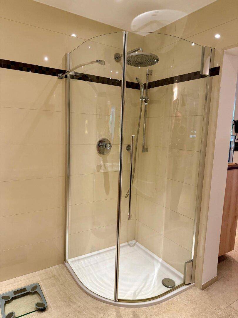 Eckduschkabine mit Glaswänden und Regendusche in einem hell gefliesten Badezimmer.