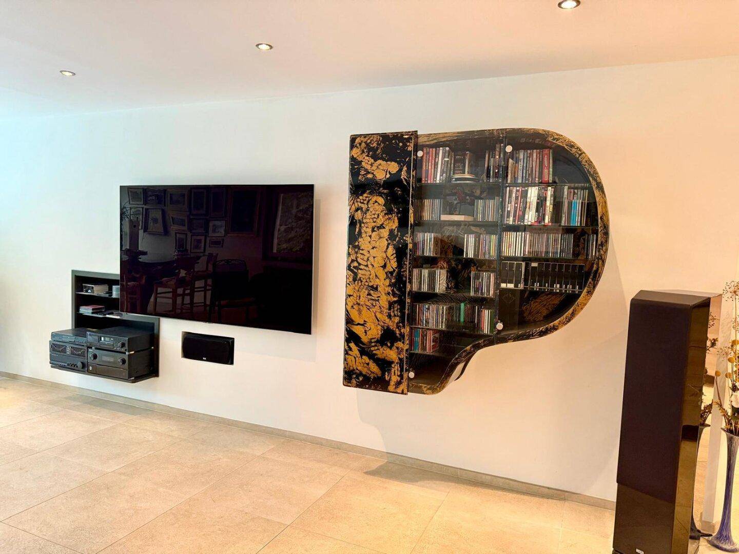 Wohnzimmer mit großem Fernseher, Wandregal in Klavierform und Fliesenboden.